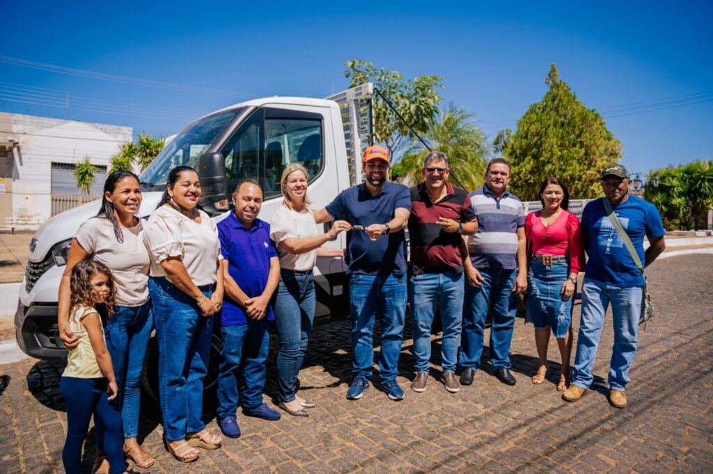 Foto com um caminhão ao fundo e pessoas ao lado do caminhão. Pedro Lucas entrega a chave do automóvel à prefeita da cidade ao lado de outras pessoas.